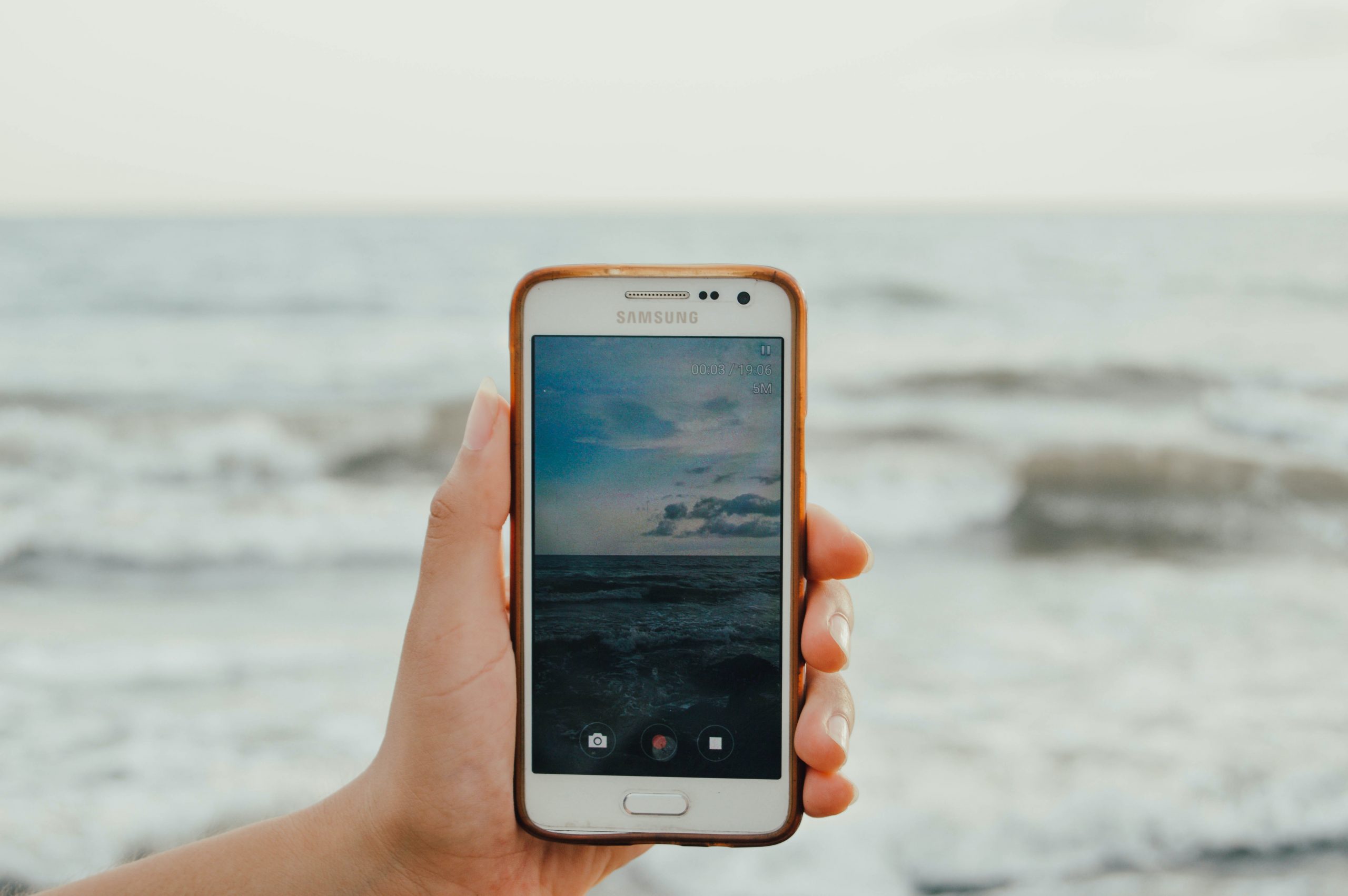 Mão com telemóvel num live streaming do mar